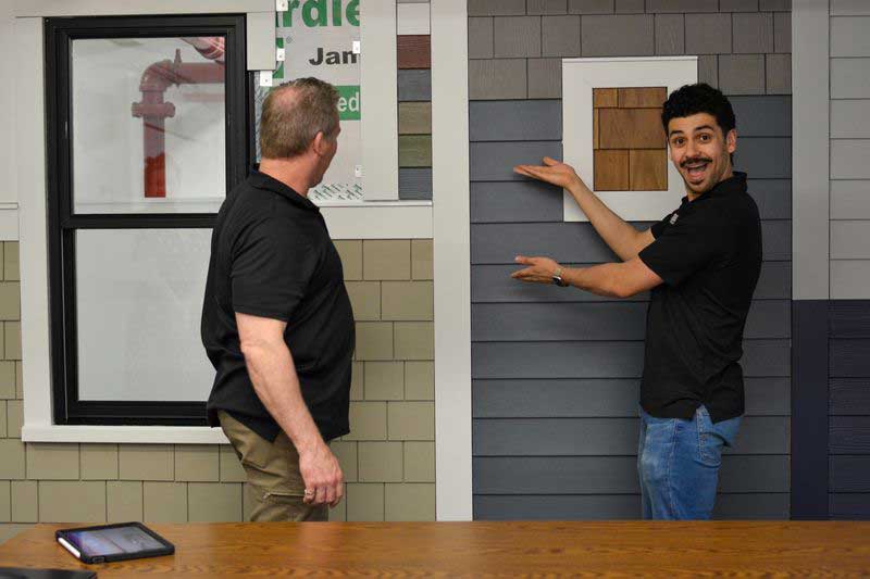 james_hardie_siding Patriot Contracting staff enthusiastically gesturing to a James Hardie siding sample wall.